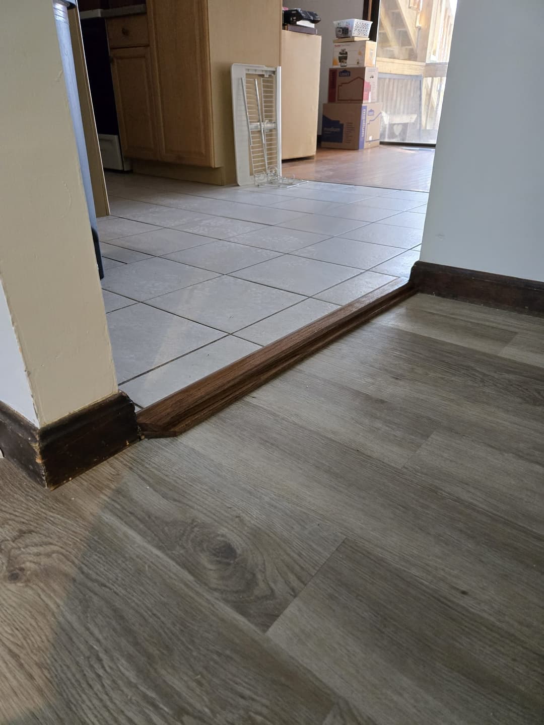 Transition from wood flooring to tiled kitchen area with boxes in background.