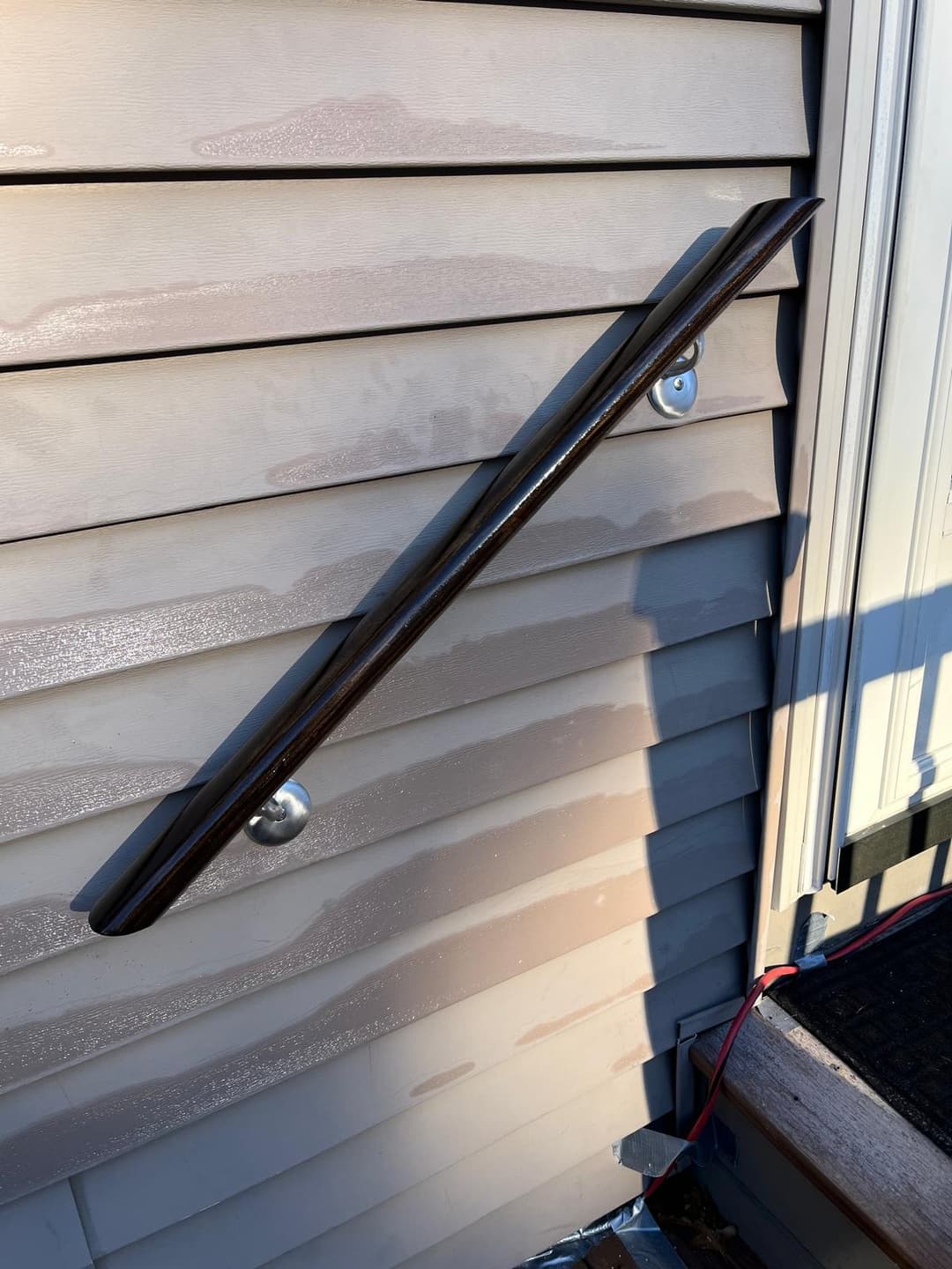 Dark wooden handrail installed on a weathered gray exterior wall with steps visible below.