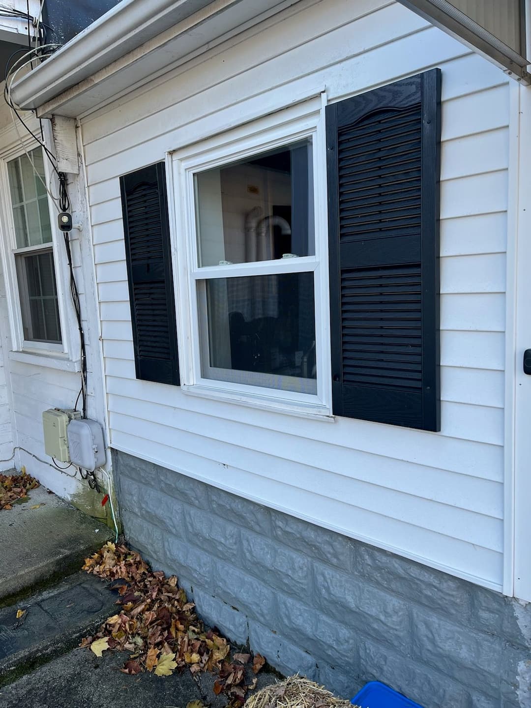 White house exterior featuring a black window with shutters and stone foundation.