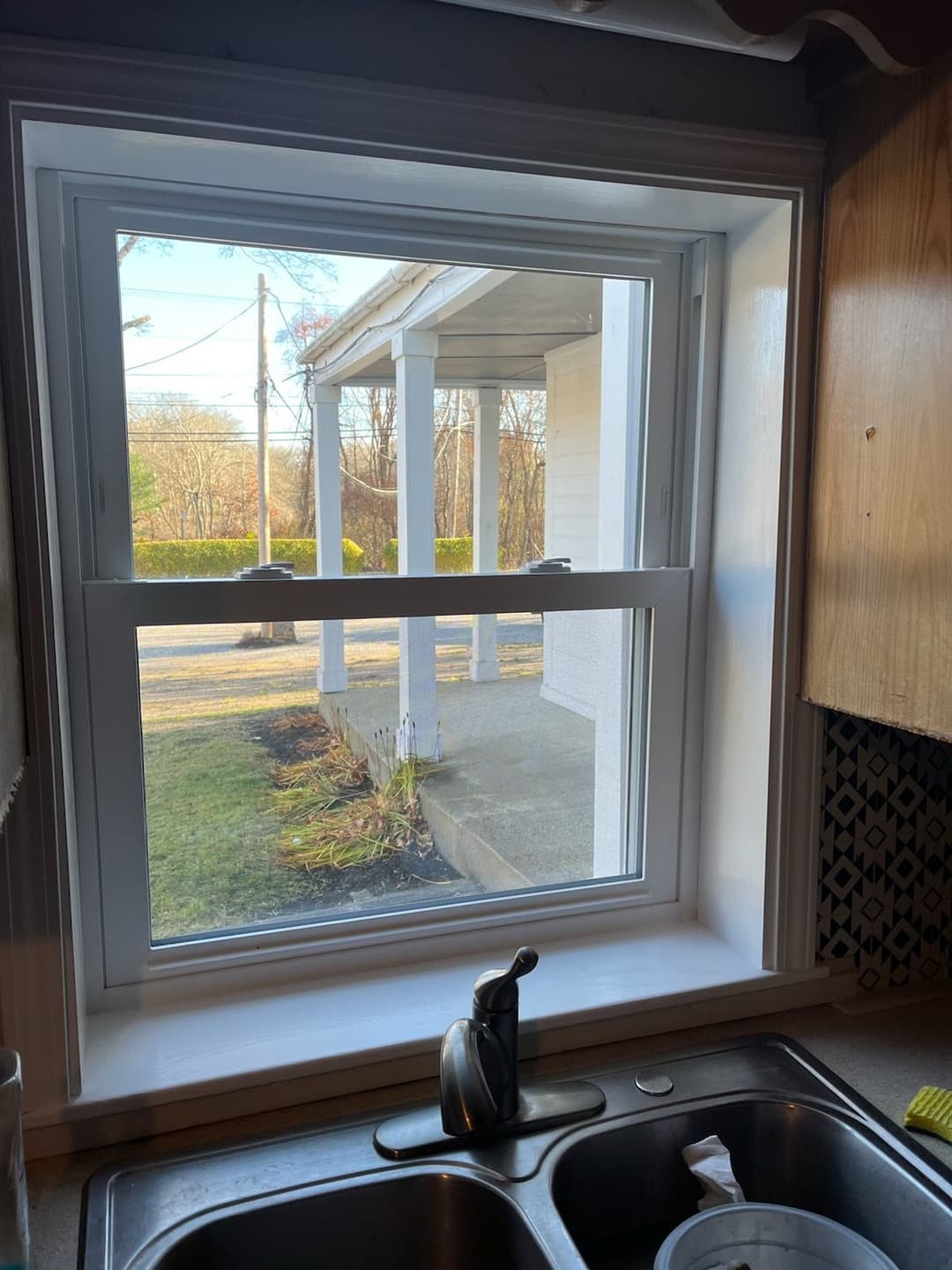 Kitchen window view overlooking a porch and garden in daylight.