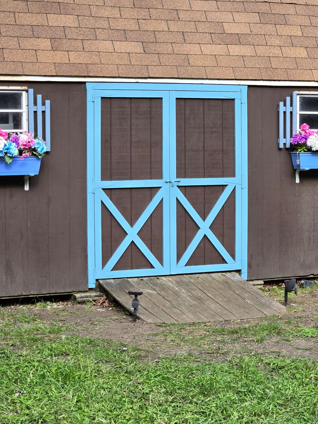 Brown barn with a blue double door and flower boxes on either side, set in a green field.